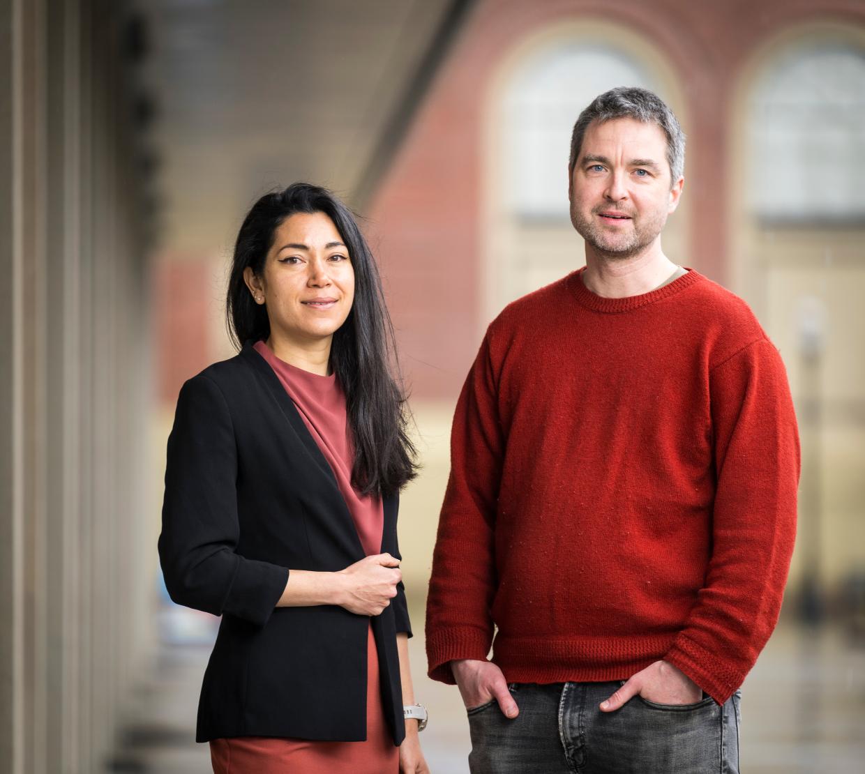 Two people stand in front of buildings.