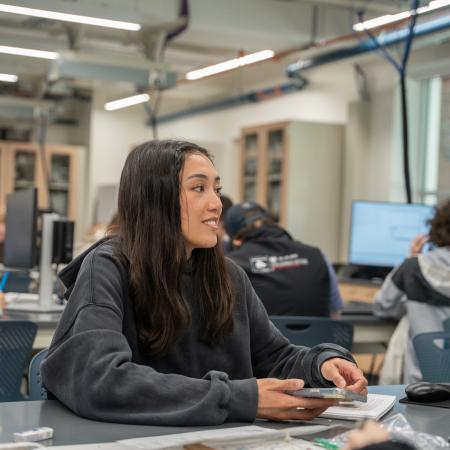 A girl in black sweatshirt works on a computer in a classroom.