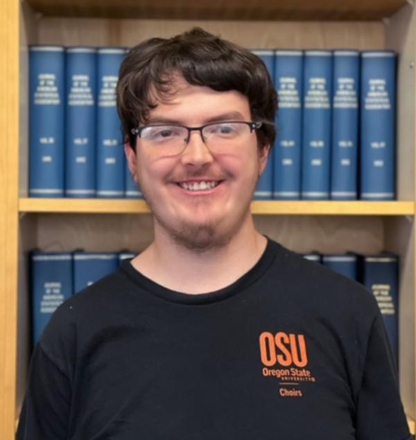 Headshot of a smiling student in front of a bookcase, wearing an OSU choir shirt