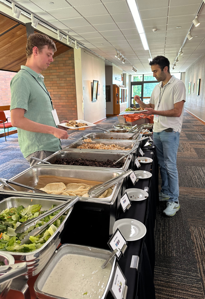 Two men finding all the necessary ingredients for tacos at a long black table full of food.
