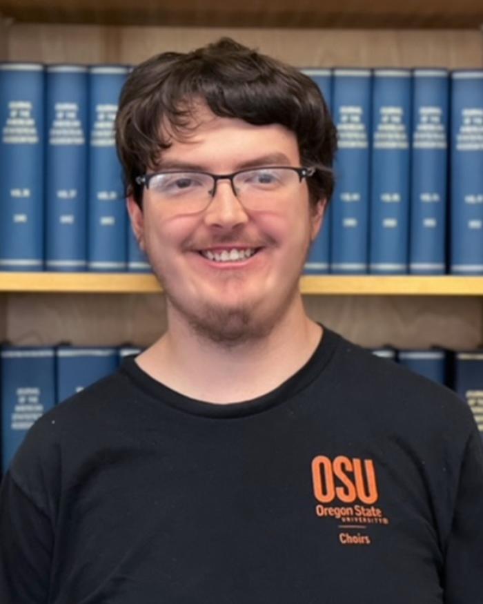 Headshot of a smiling student in front of a bookcase, wearing an OSU choir shirt