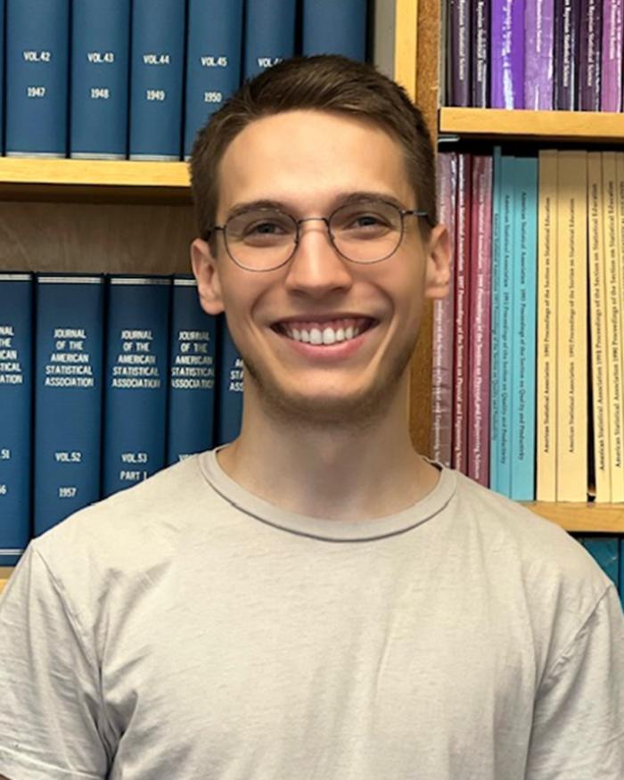 Headshot of a smiling student standing in front of a bookshelf