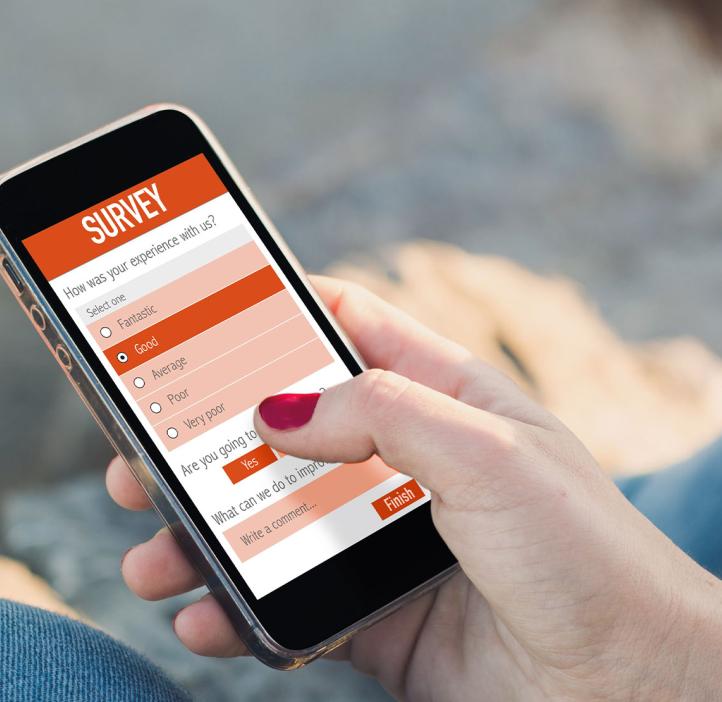 A hand with pink painted thumbnail uses a phone with an orange survey on the screen.