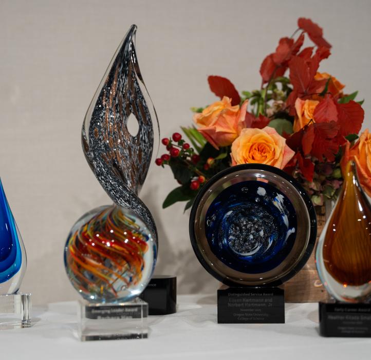Display of colorful circular glass awards on a table with an orange floral centerpiece at the College of Science Alumni Awards Ceremony.