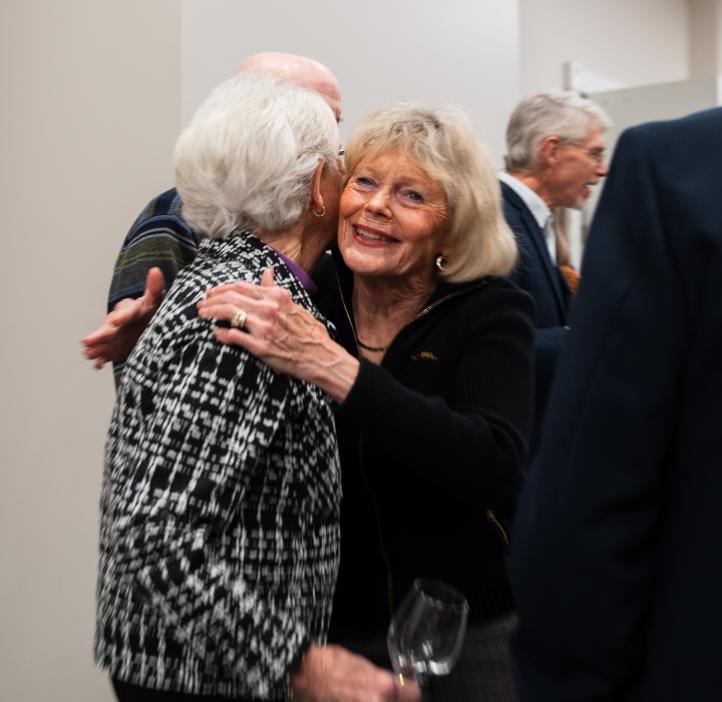 Two attendees greet each other warmly at the College of Science Alumni Awards Ceremony, holding a wine glass.