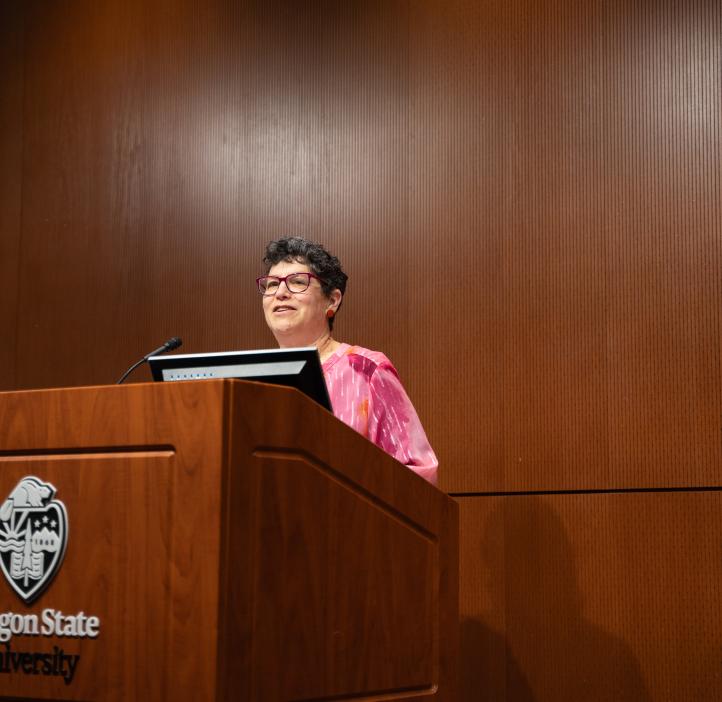 A woman in a pink blazer talks at a podium.